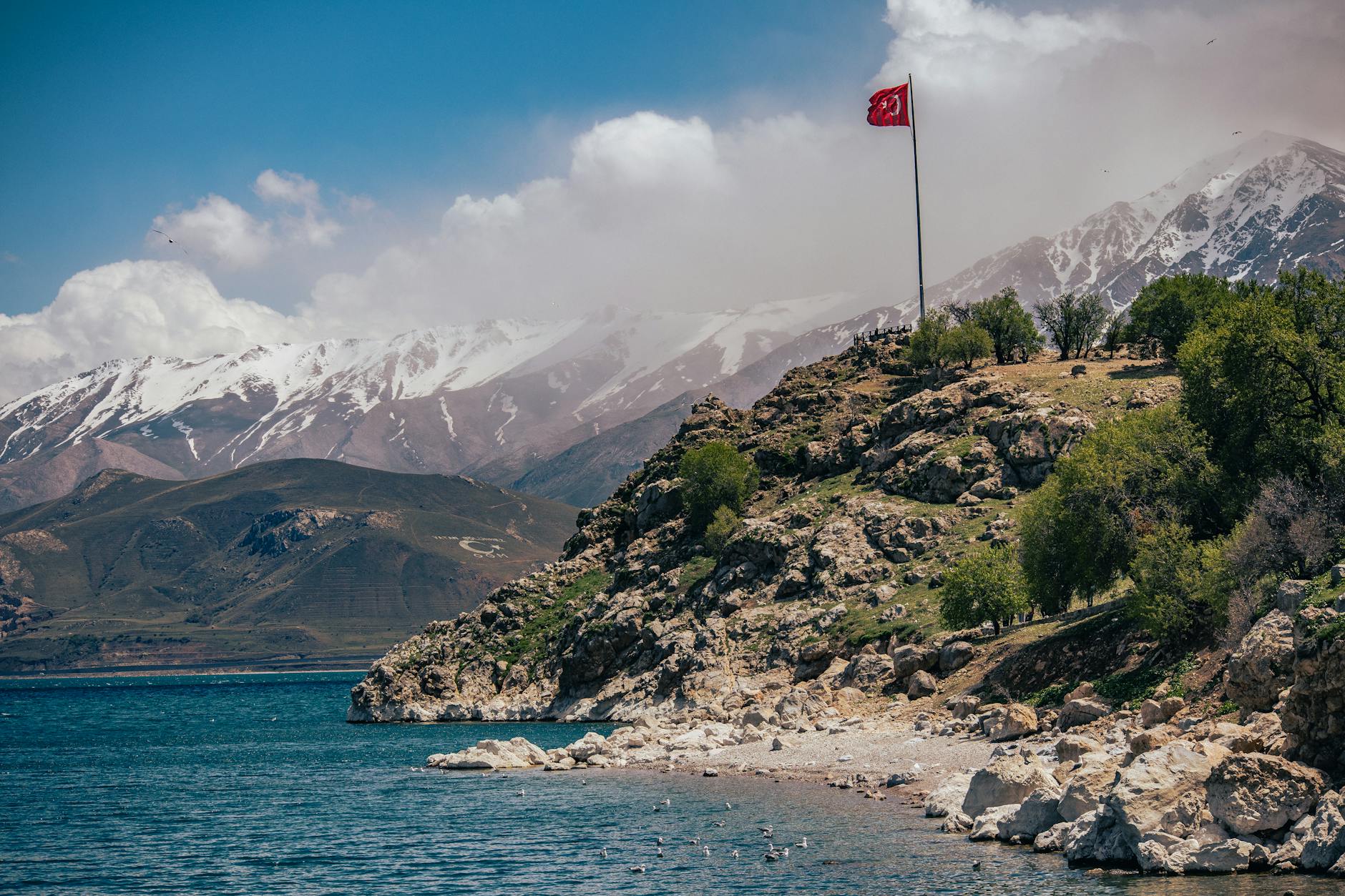 a turkish flag on a pole on the shore with the view of mountains